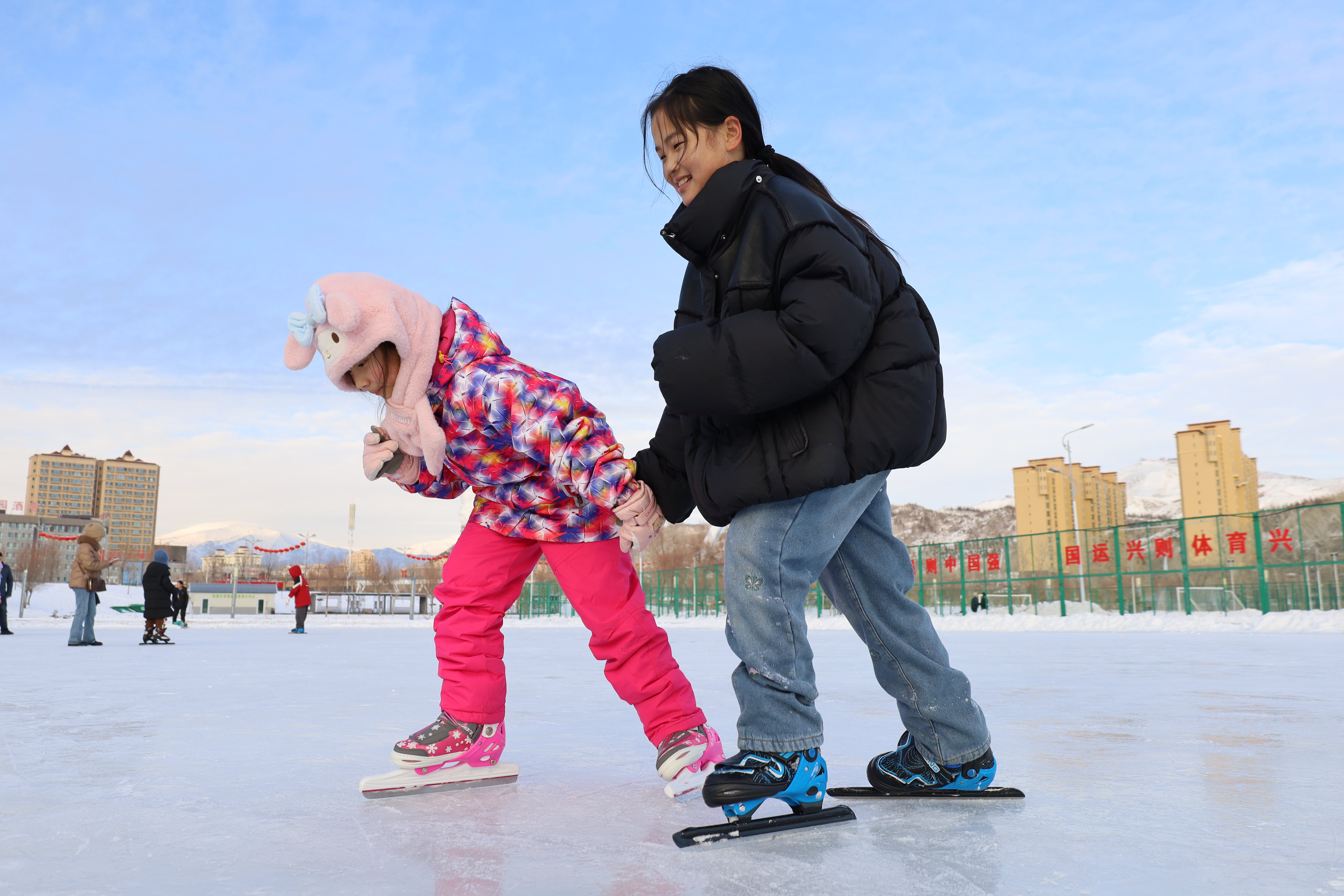 在滑冰场内,小朋友们手拉手滑冰,尽享冰雪运动的欢乐。